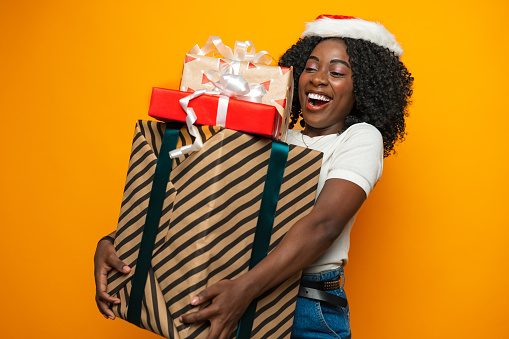 Beautiful african girl with Christmas gift standing against yellow background in studio