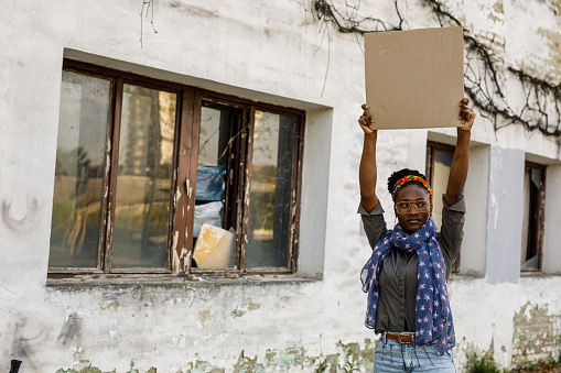 Copy space shot of serious young Black woman standing on the city street, holding up a cardboard with copy space, protesting for a cause.