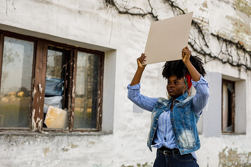 Copy space shot of confident young Black woman standing on the city street, holding a cardboard cut out and protesting for a social cause.