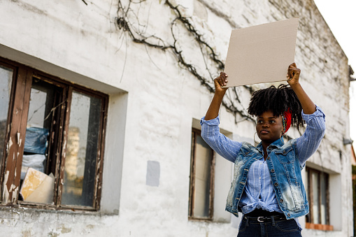 Copy space shot of confident young Black woman standing on the city street, holding a cardboard cut out and protesting for a social cause.