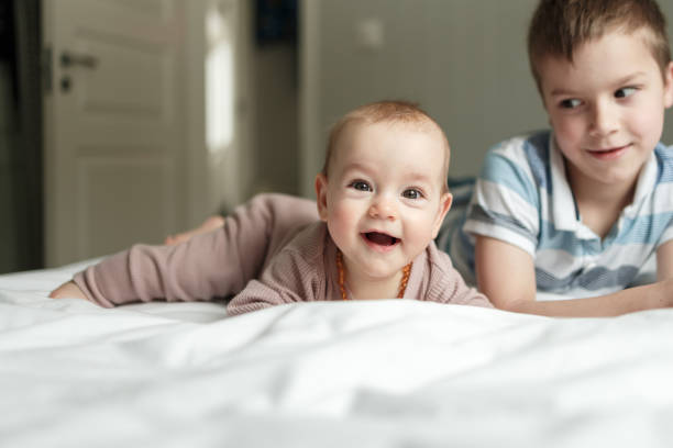 Brother and his baby sister on the bed at home stock photo