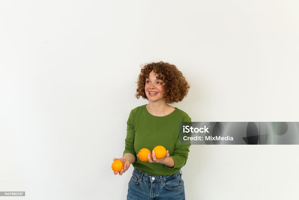 Studio portrait of a cheerful girl juggling with oranges Studio portrait of a beautiful, young redhead woman holding a bunch of oranges 30-34 Years Stock Photo