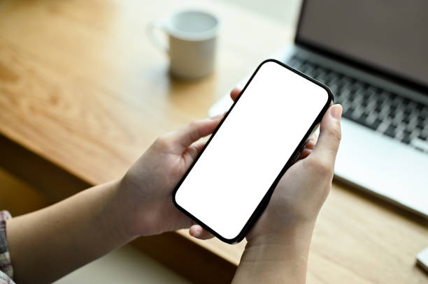 istock A smartphone white screen mockup is in a woman's hands over modern office desk. top view 1447884200