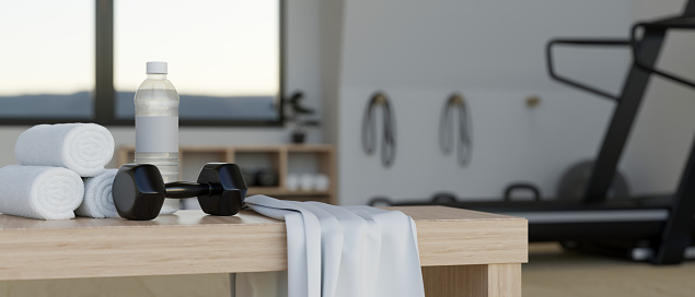 Dumbbell, a bottle of water and towels on a bench in modern fitness gym. Sport equipments with fitness in the background. 3d rendering, 3d illustration