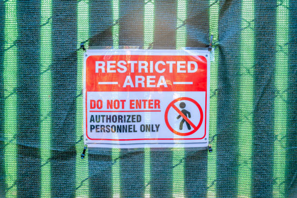 Restricted area do not enter signage in San Francisco, California. Close-up of a DO NOT ENTER sign against the cloth with a shade of chain link fence with privacy strips at the back.