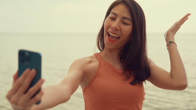 Young Asian woman using smartphone taking a selfie on tropical beach.