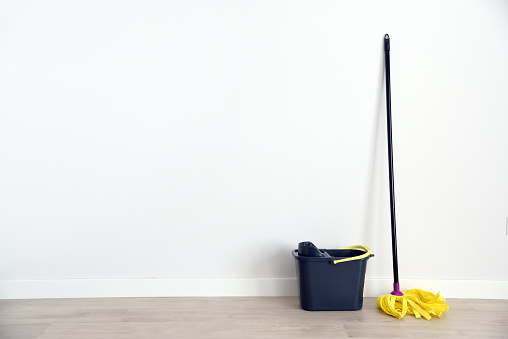 A mop and a gray bucket in front of a white wall in an empty room.