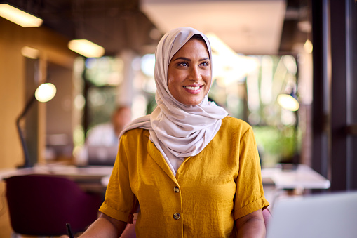 Mature Businesswoman Wearing Headscarf Working On Laptop At Desk In Office