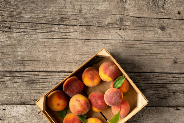 Peaches in a box on a wooden background top view.