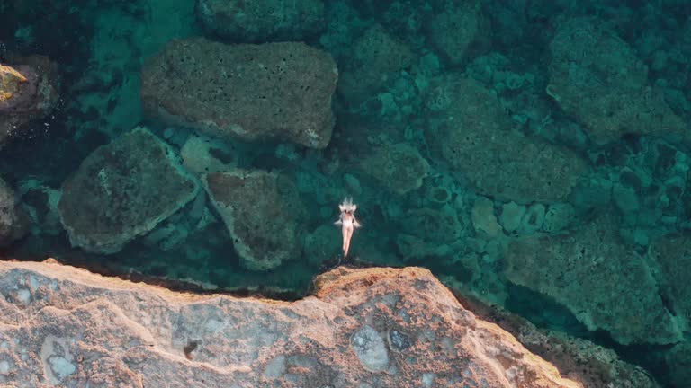 Drone shot of a young woman jumping and swimming on the sea