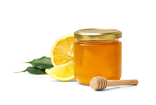 Honey in a glass jar and lemon with leaves on a white background. Closed jar with honey and honey stick on isolation