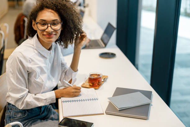 istock Smiling woman freelancer working laptop and making notes while sitting near windows in cozy cafe 1447893273
