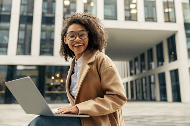 Smiling african business woman working laptop while sitting outside on background of office building