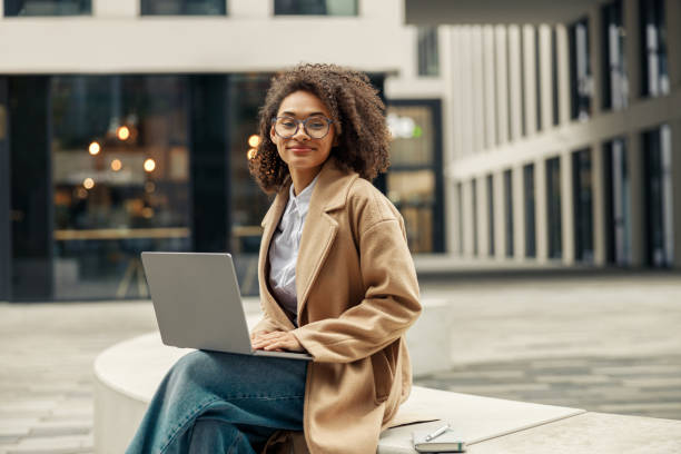 Happy african business woman working laptop while sitting outside on background of office building