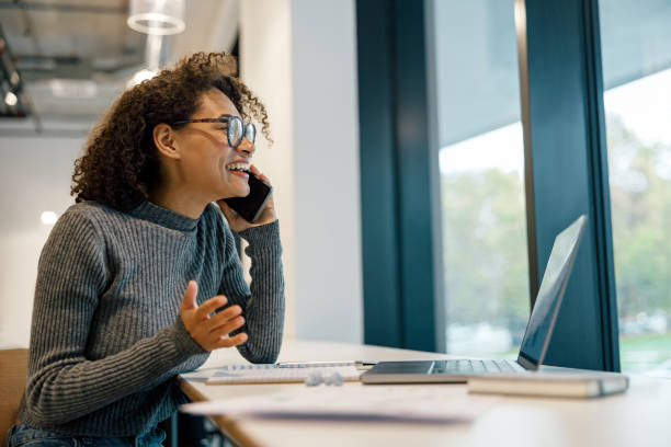 istock Smiling woman freelancer working laptop and talking phone while sitting in cozy coworking 1447896172