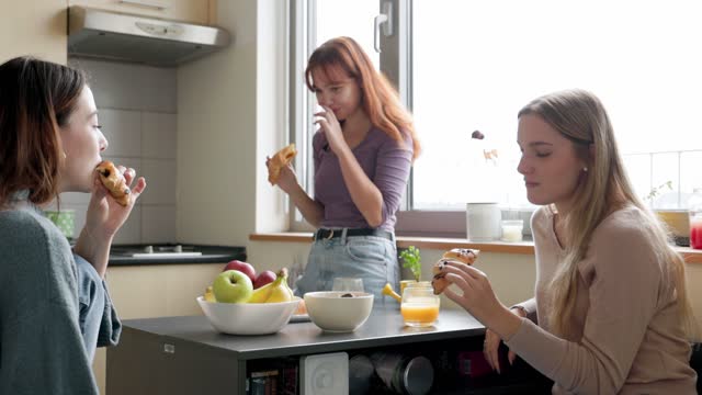 Three women students having a snack, chocolate croissants, in the dorm room kitchen