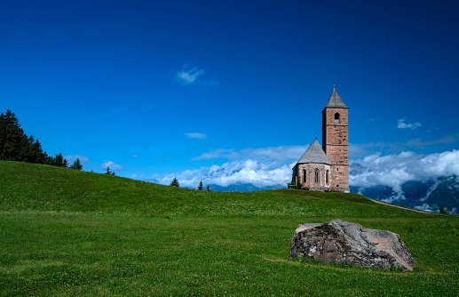 Small old wooden chapel on summer green grassy hill top, lonely willow tree and blue sky with cloud.