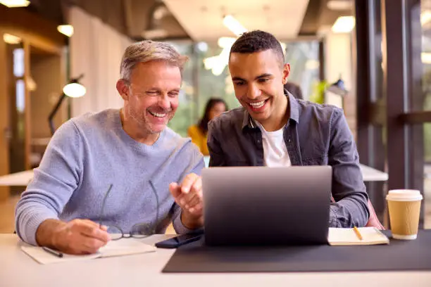 Photo of Mature Businessman Mentoring Younger Colleague Working On Laptop At Desk