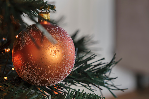 Closeup of a frosted bronze orange brown colored christmas ball in an artificial christmas tree. Image with copy space.