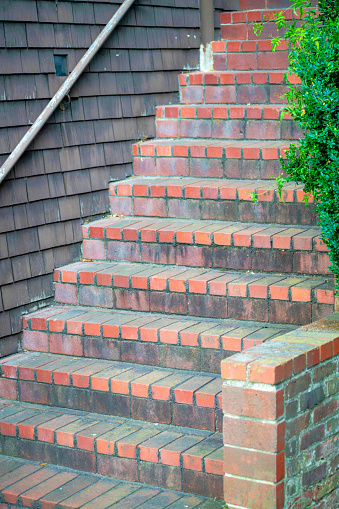 Row of red brick stairs with decorative cement on a house or home entry near front door with black metal gaurd hand rail. Front yard bushes in the downtown city neighborhoods in suburban area.