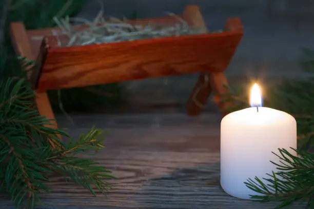 Photo of Burning candle and christmas manger in background, prayer and waiting for coming of Jesus concept