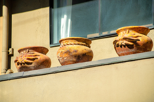 Row of decorative clay pots with house or home background beige color in the late afternoon sun in a suburban area. In the city or in the downtown neighborhood with visible window on porch.