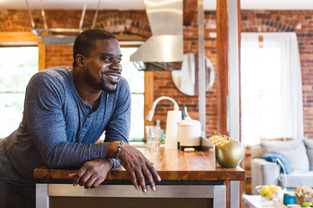 istock Charming Black man leaning against the kitchen counter, smiling and contemplating 1447903606