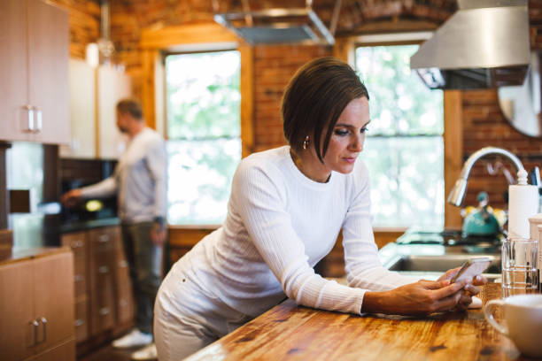 istock Woman leaning against the kitchen counter and using smart phone 1447903693