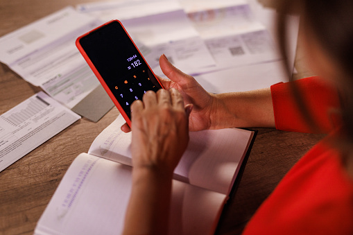 Close up shot of woman sorting out expenses, bills and finances at home and using a calculator on her smart phone to see how much money is at her disposal.