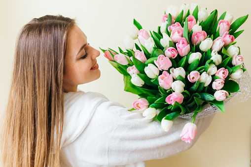 Cheerful young lady with long hair being excited to get bouquet of pink tulips on women's day isolated over white background.