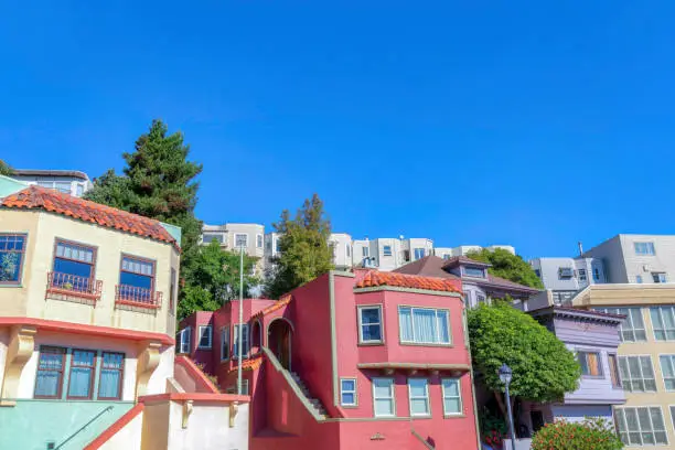 Rowhouses and apartment buildings facade in San Francisco, CA. There are houses at the front with colorful wood sidings and stairs leading to the front doors and apartment at the back.