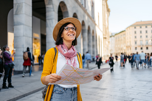 Beautiful young female tourist using a map on town square in Milan, Italy.