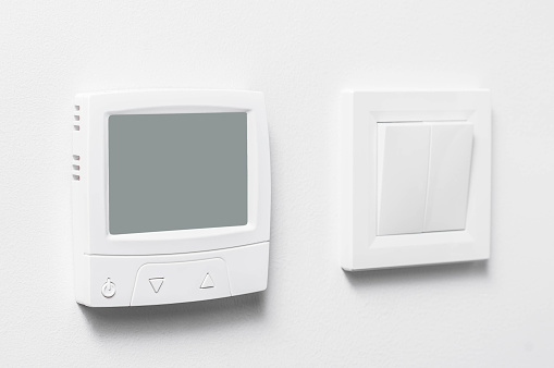 Floor heating control unit and light switch on a white wall with space for copy space