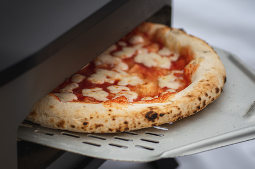 Cooking or baking hot pizza Margherita with tomato sauce and mozzarella cheese with a shovel in an electric or gas oven, with smoke, close up