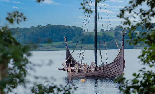 Viking boat replica moored with no people at close-by Lake Fårup. Decorated shields are visible at the side of the boat. The city Jelling is an ancient Royal Residence location.