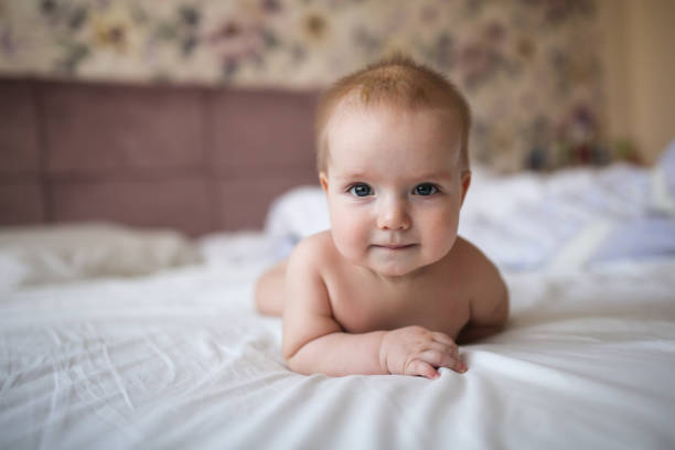 baby of 6 months is lying on bed in bright real charming baby of 6 months is lying on his stomach on a bed in a bright real interior, with the end of childhood and healthy development half dozen babies stock pictures, royalty-free photos & images