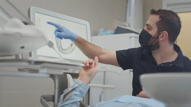 A male orthodontist doctor scans a man's teeth and jaw in the clinic's medical office. Creates a 3d model with an intraoral manual 3d scanner. Diagnosis of caries