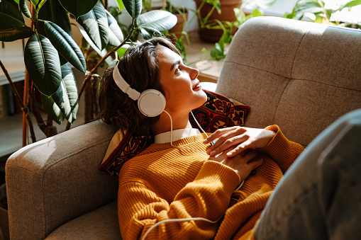 Brunette young woman listening music while resting on couch at home