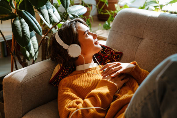 Brunette young woman listening music while resting on couch stock photo