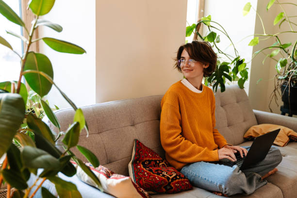 istock Brunette young woman working with laptop while sitting on couch 1447935055