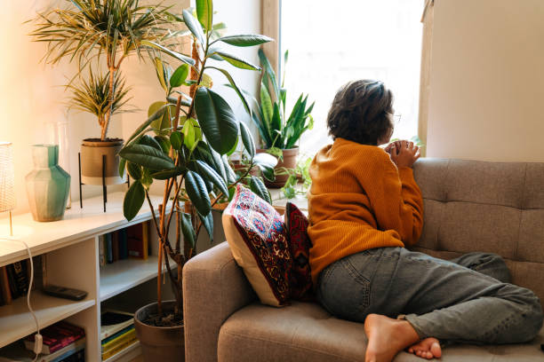 istock Brunette young woman looking in window while sitting on couch 1447935089