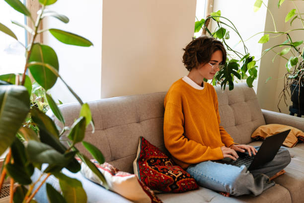 istock Brunette young woman working with laptop while sitting on couch 1447935865
