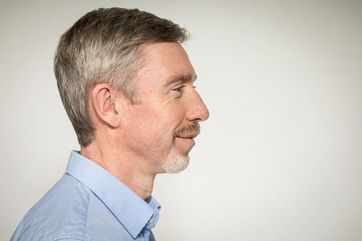 Close-up studio portrait of a 50 year old white bearded man in a blue shirt  against a white background