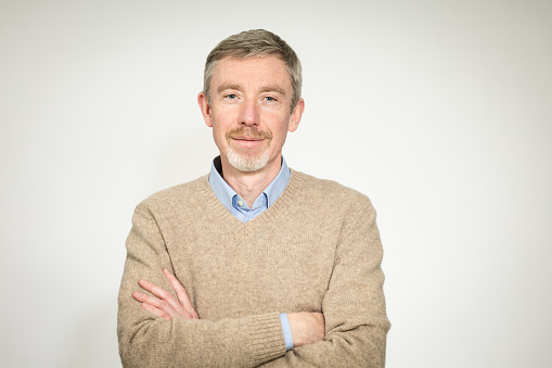 Studio portrait of a 50 year old white bearded man in a beige sweater against a white background