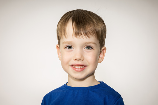 Close-up studio portrait of a 5 year old white cheerful boy in a blue t-shirt against a white background