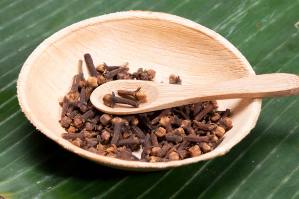 Dried cloves in the wooden bowl, on a bamboo leaf. stock photo