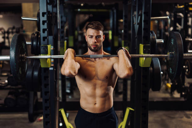 Muscular shirtless male bodybuilder lifting a barbell at the gym stock photo