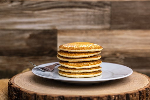 A large plate stack of pancakes with a fork against a wood background plain with no syrup.