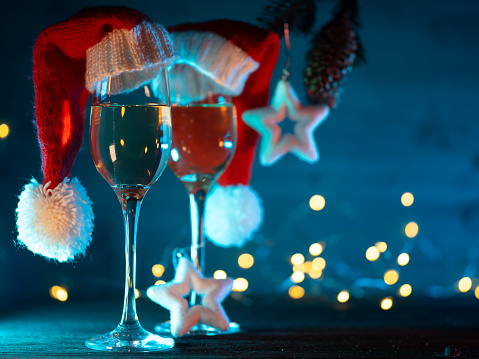 two glasses of champagne in Santa hats on a blue background with a Christmas tree branch and cones