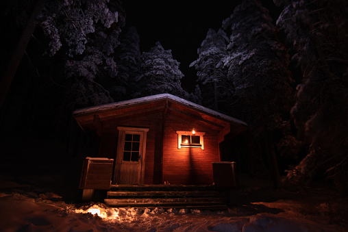 Winter scene with remote cabin illuminated by candlelight in the forest